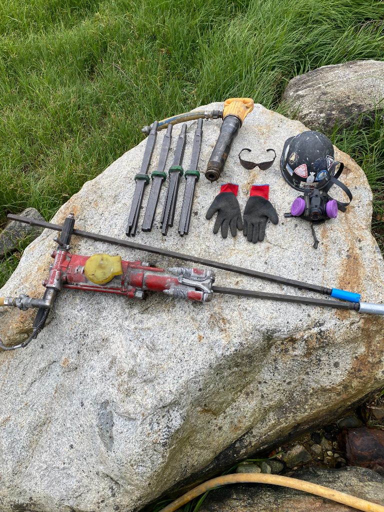 Pneumatic drill and rock breaking tools laid out on granite